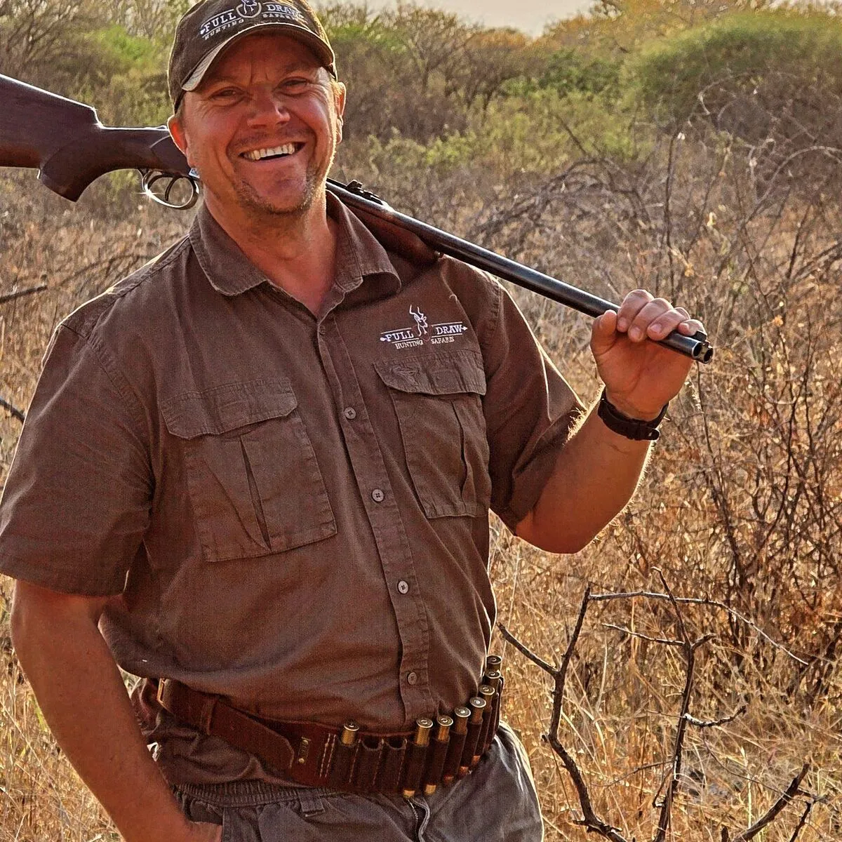 A smiling Full Draw guide with a rifle over his shoulder in the bushveld